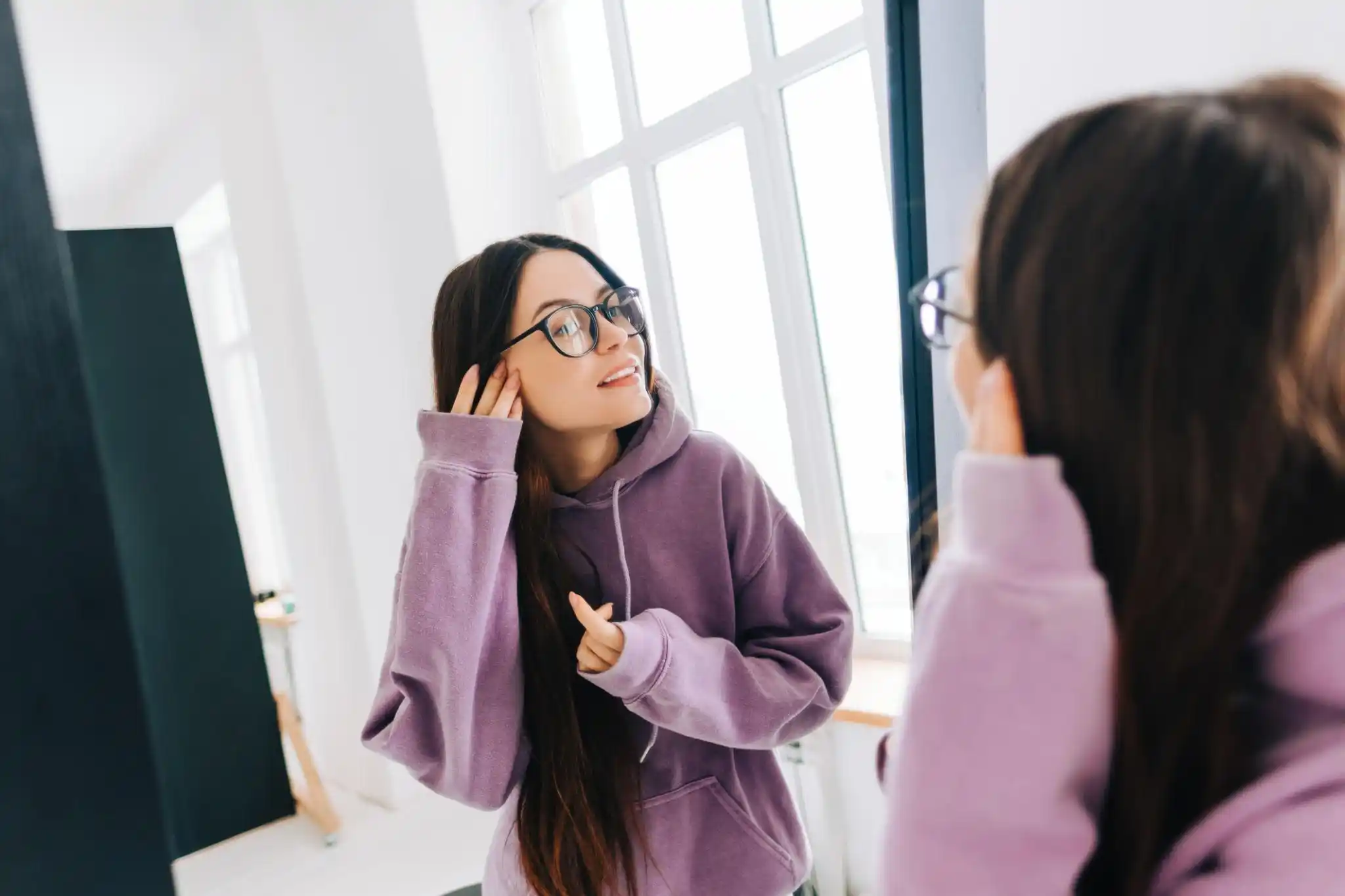 Femme essayant ses nouvelles lunettes devant un miroir pour vérifier leur confort et leur apparence